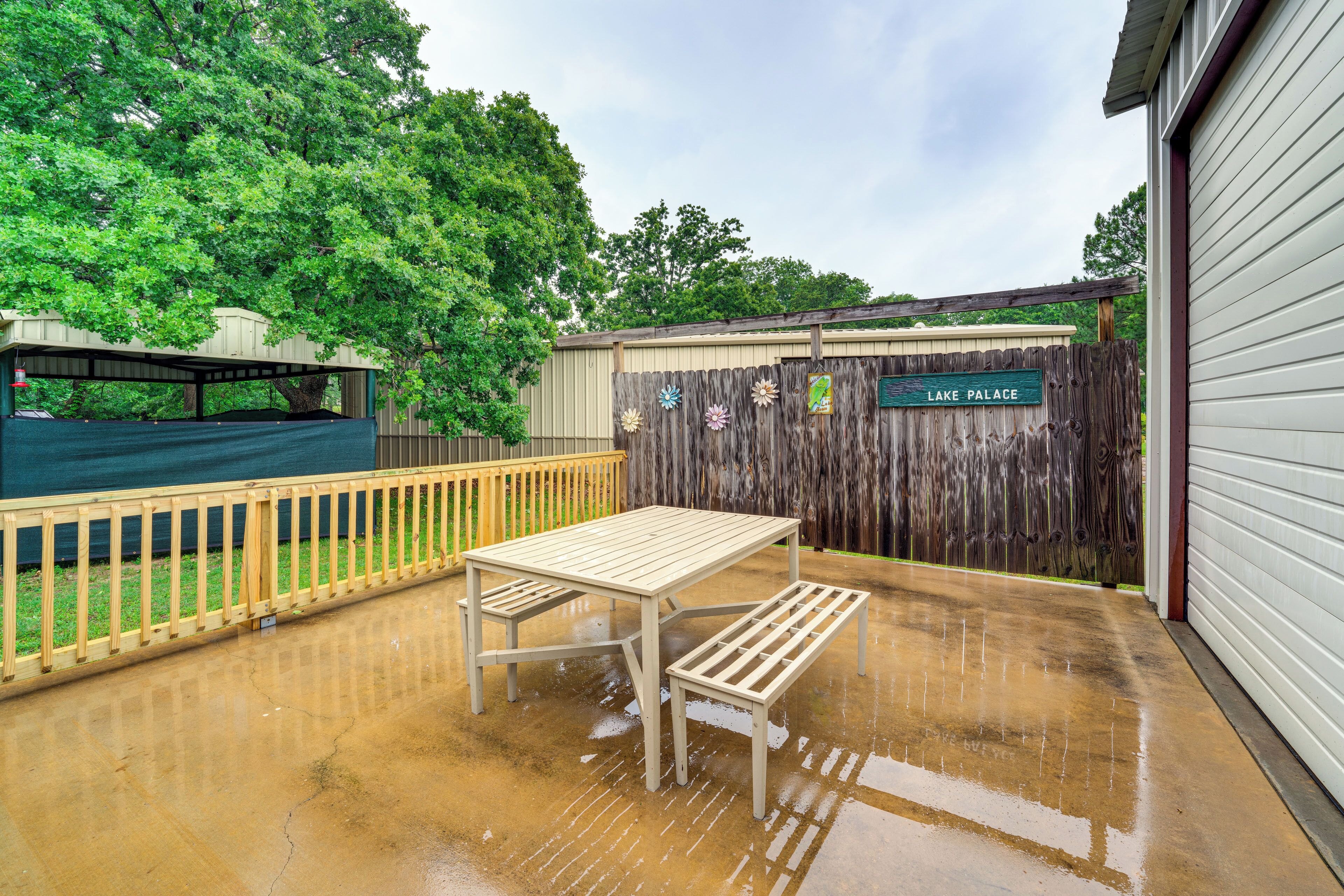 A covered patio area with a wooden table and bench, a wooden fence, and a sign that reads "Lake Palace."