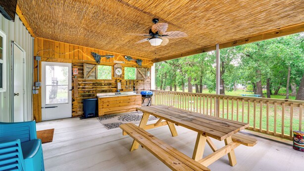 Eine Holzterrasse mit Picknicktisch und Bänken, einem Deckenventilator und Blick auf die umliegenden Bäume.