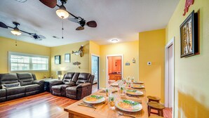 Ein geräumiges Wohnzimmer mit einem Holzespeisetisch, der für eine Mahlzeit gedeckt ist, Ledersofas und Deckenventilatoren.