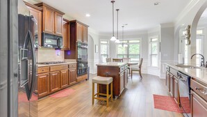 A modern kitchen with wooden cabinets, stainless steel appliances, and a central island with stools. - 9 Mi to Trilith Studios: Gem in Fayetteville! (Fayetteville)