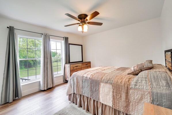 A bedroom with a large window, a ceiling fan, and a bed with a quilted bedspread.