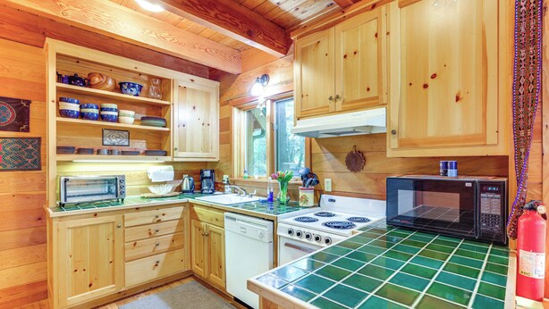 A wooden cabin kitchen with a green-tiled countertop, wooden cabinets, a stove, a microwave, and a dishwasher.