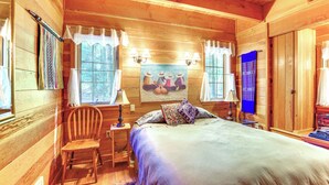 A wooden cabin bedroom with a bed, a chair, a nightstand, and a window with curtains.