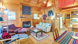 A cozy cabin interior with a fireplace, wooden furniture, and a dining area.
