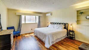 A bedroom with a large bed, wooden flooring, a window with curtains, a dresser, and a bedside table with a lamp. - Walkable Townhome: 'M on Main' in Wytheville (Wytheville)