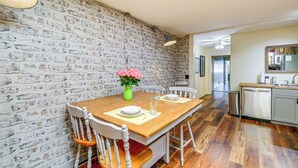 A dining area with a brick wall, wooden table, white chairs, and a vase of flowers. - Walkable Townhome: 'M on Main' in Wytheville (Wytheville)