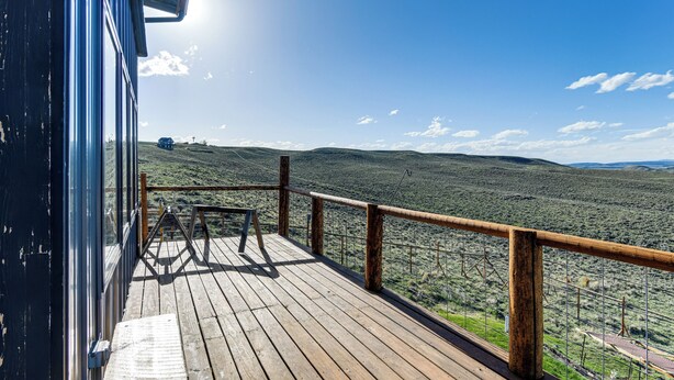 Eine Holzterrasse mit Metallgeländer, das auf eine hügelige Landschaft blickt.