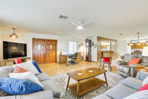 A spacious living room with a large flat-screen TV, a wooden dining table, and a comfortable seating area with sofas and a rocking chair.
