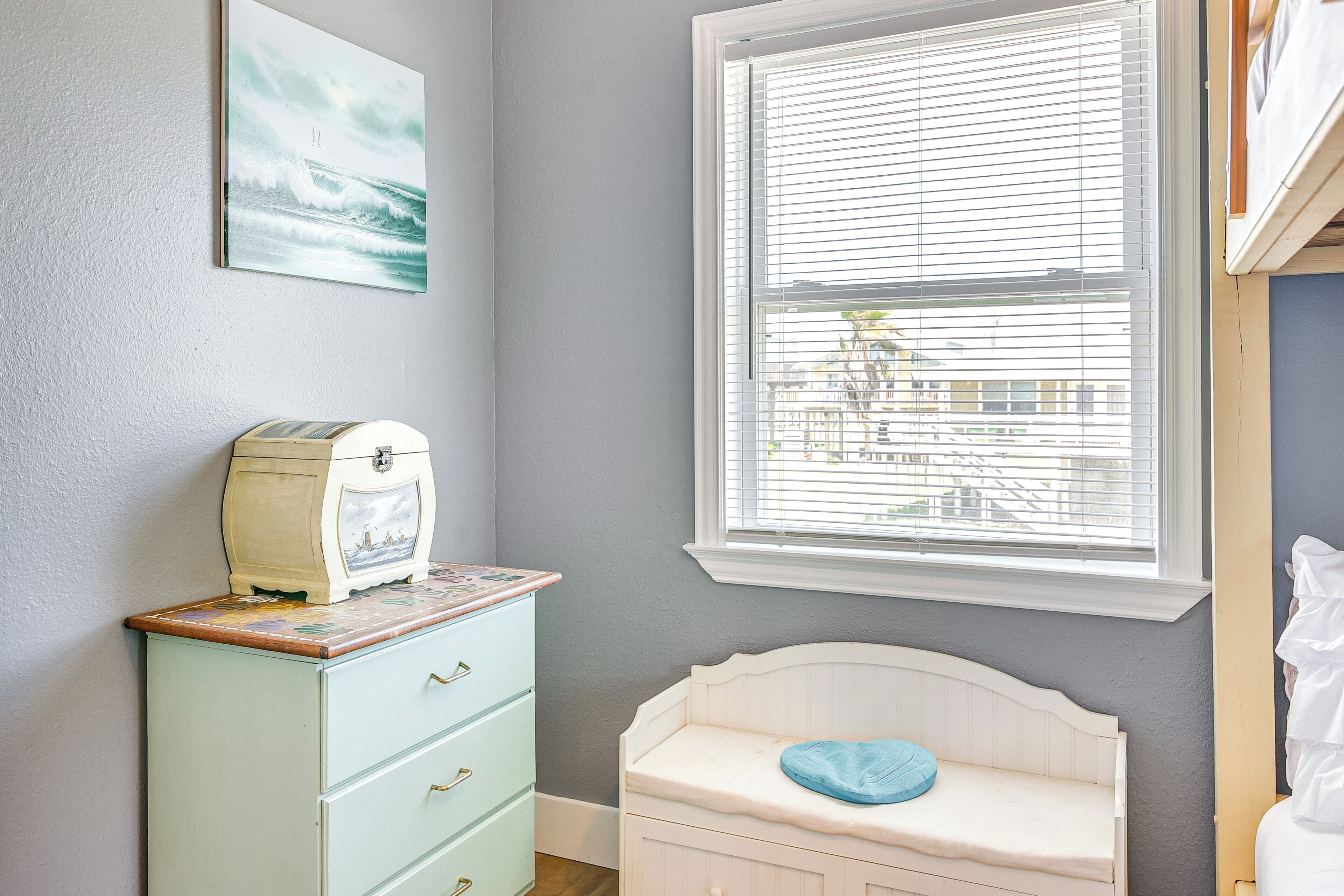 A room with a light blue dresser, a white crib, a window with blinds, and a wall-mounted picture.