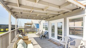 A covered porch with wicker furniture and plastic chairs, overlooking a beach. - Walk to Beach: Family Getaway By San Luis Pass! (Freeport)