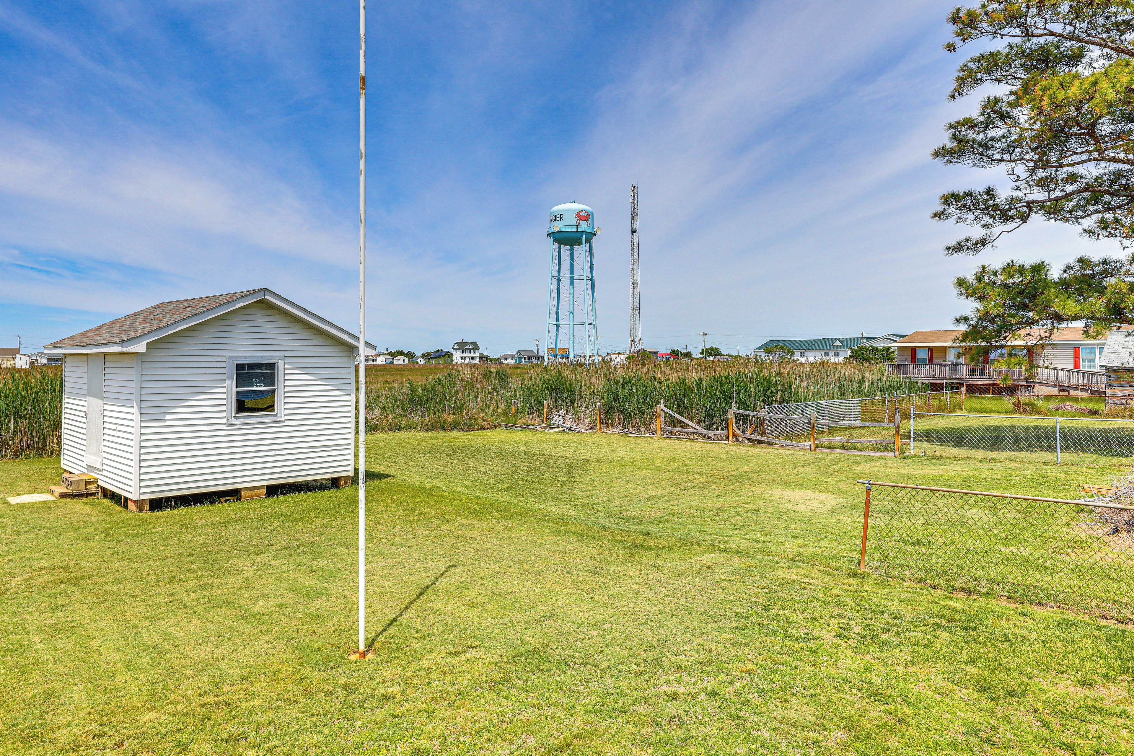 A small white house with a sloped roof, a water tower in the background, and a grassy area with a fence.