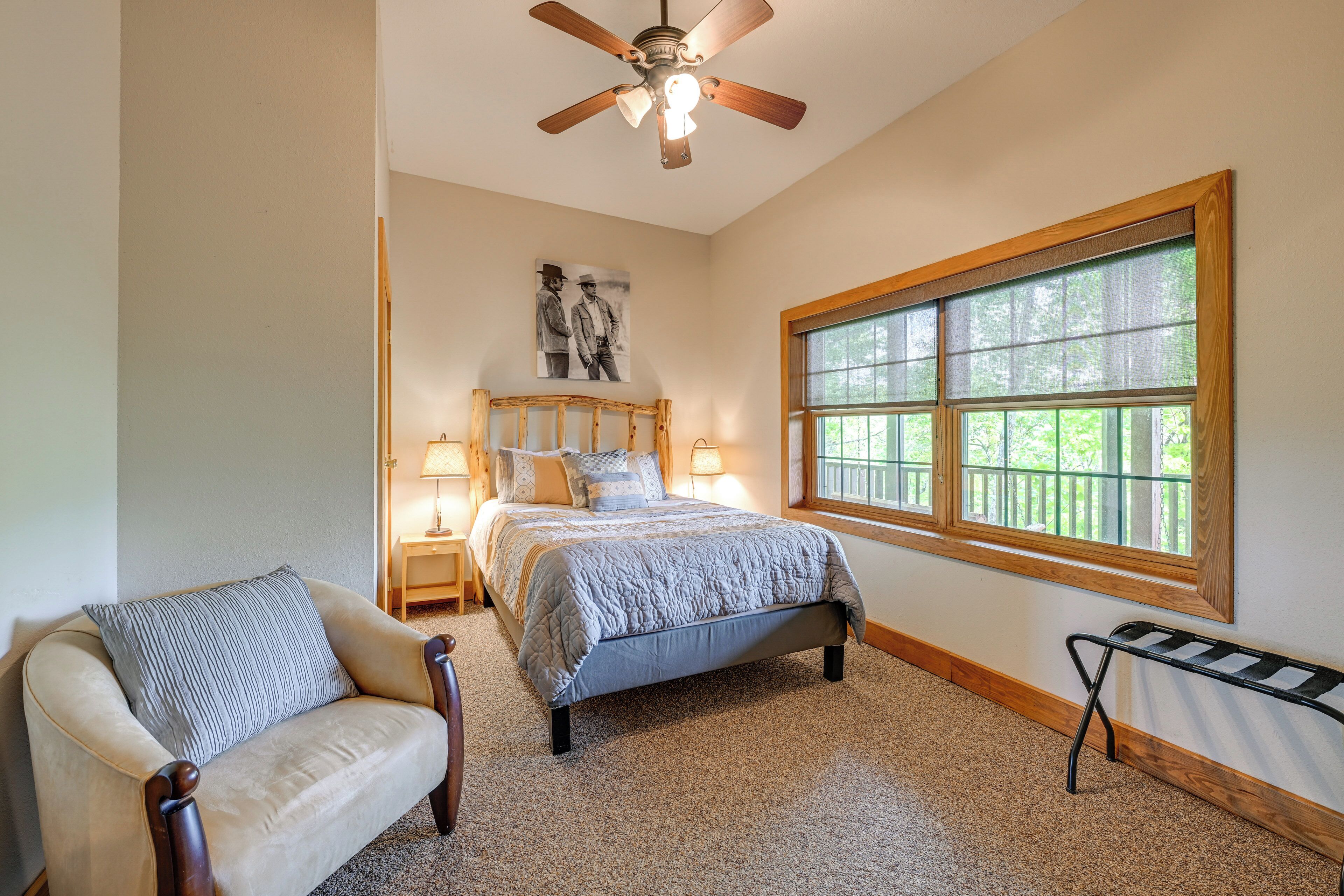 A bedroom with a bed, a chair, a nightstand, a lamp, a window, and a ceiling fan.