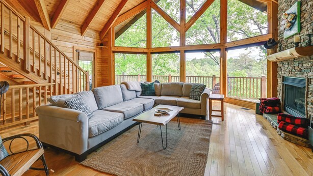 A spacious living room with a wooden ceiling, large windows, a stone fireplace, and a cozy seating area. - Game Room, Hot Tub & Decks: Scenic Franklin Cabin (Franklin)