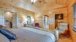 A wooden cabin interior with a bed, a chair, a television, and a ceiling fan. - Game Room, Hot Tub & Decks: Scenic Franklin Cabin (Franklin)