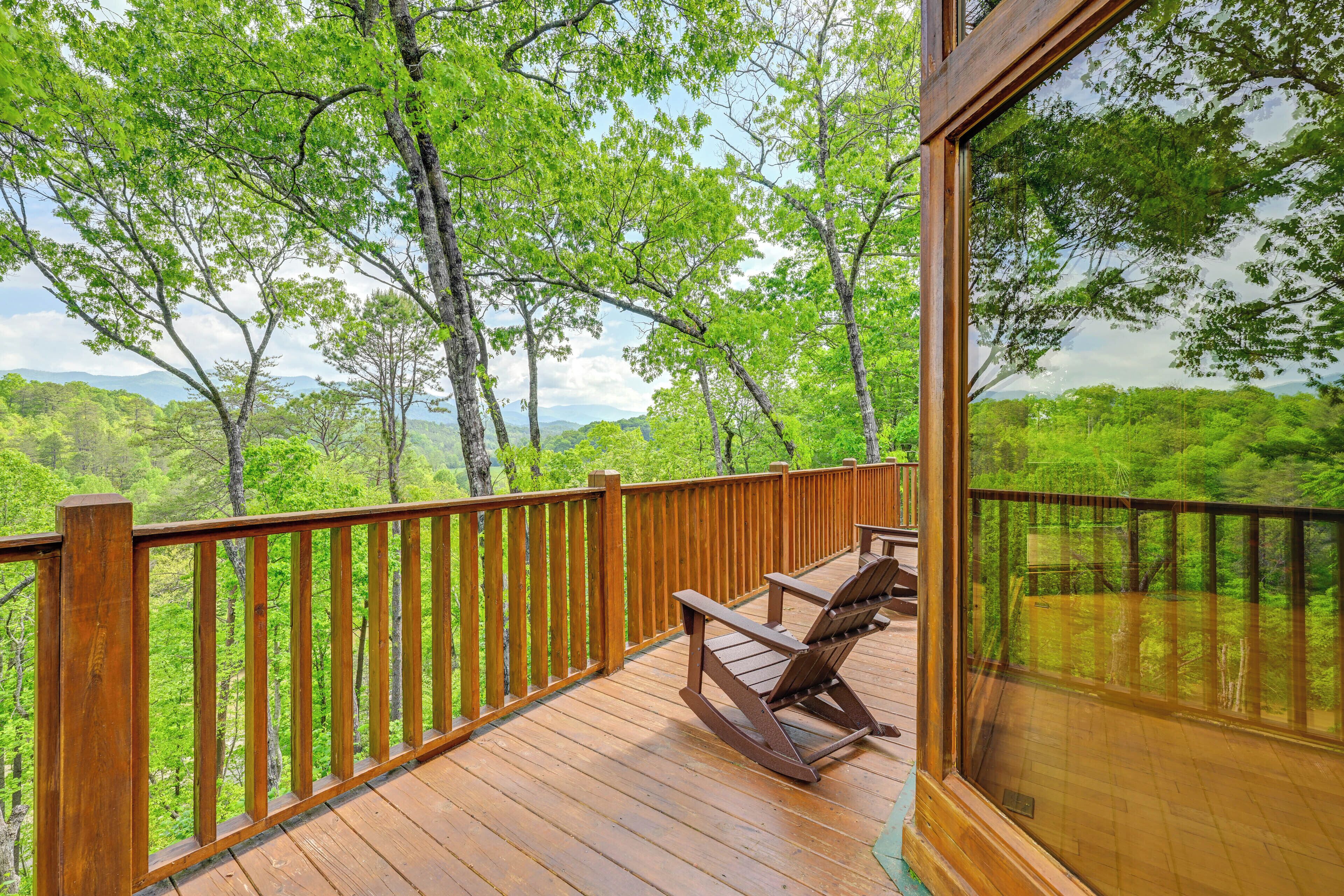Eine Holzterrasse mit einem Schaukelstuhl, mit Blick auf eine üppige, grüne Landschaft mit Bäumen und entfernten Bergen.