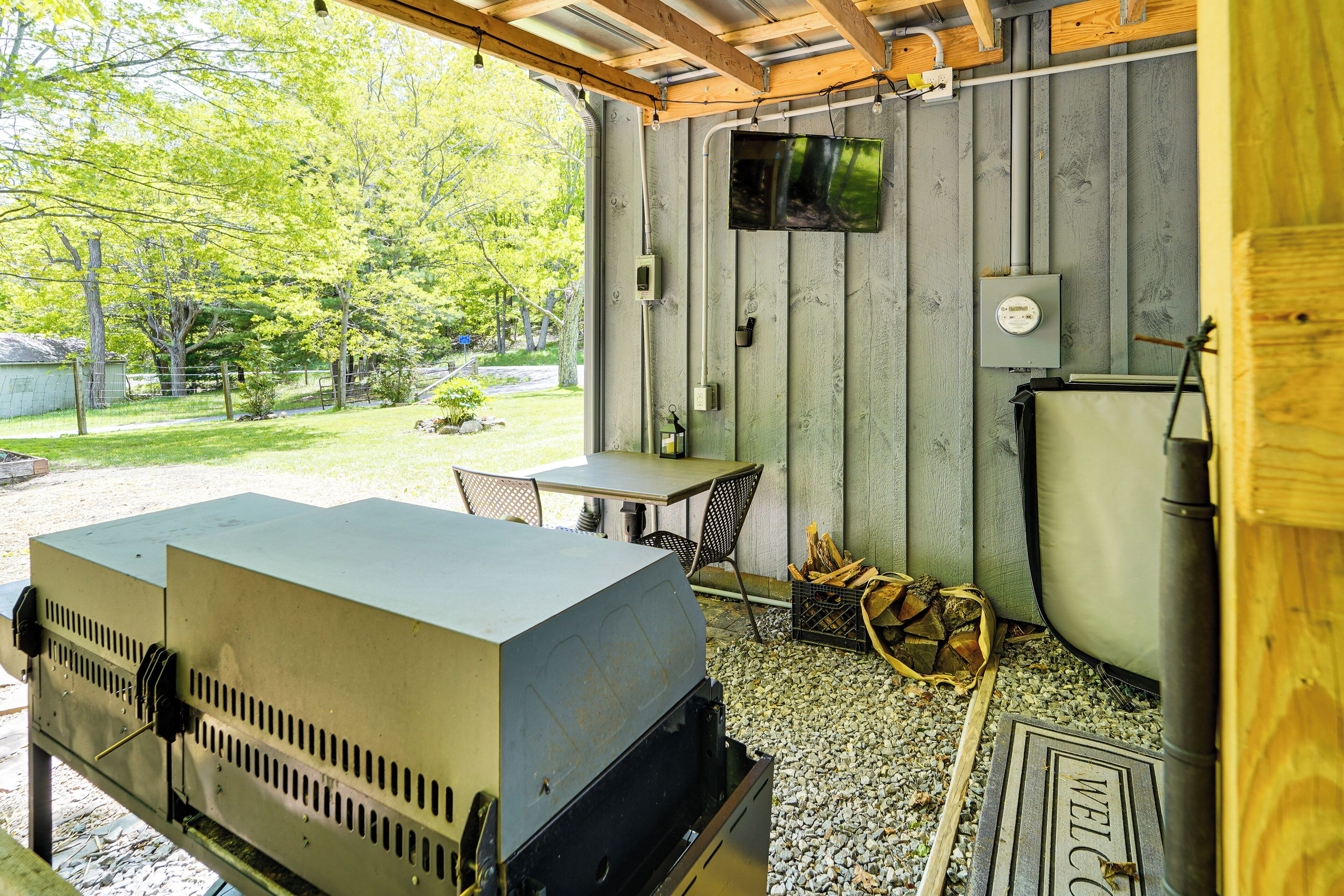 A covered outdoor area with a grill, a table, chairs, and a television mounted on the wall.