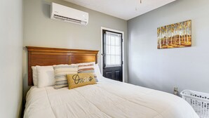 A bedroom with a bed, a door with blinds, a wall-mounted air conditioner, and a painting. - Hike to Fire Tower! Monterey Cabin on 4 Acres (Monterey)