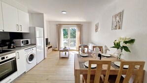 A modern kitchen with white cabinets, a microwave, a washing machine, and a dining area with a wooden table and chairs. - COMPLETE APARTMENT WITH TERRACE (Mondariz)