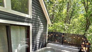 Un jacuzzi al aire libre con escalones, rodeado por una terraza de madera y una valla metálica, con árboles al fondo.
