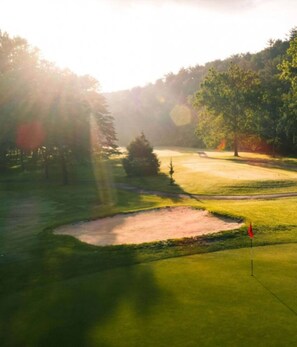 A golf course with a sand bunker, trees, and a flagstick.
