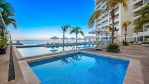 A pool area with lounge chairs and umbrellas, a clear sky, and a view of the ocean. - Panoramic Hot Tub Oceanview Luxury 4BR Penthouse (Puerto Vallarta)