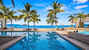 A pool area with lounge chairs and palm trees, overlooking a body of water. - Gorgeous 1BR Condo With Pools Sea Views (Puerto Vallarta)