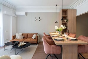 A modern living room with a brown sofa, a black coffee table, and a wooden dining table set for six.