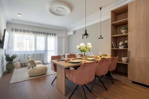 A modern dining area with a wooden table, pink chairs, and a central white pouf.