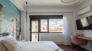 A bedroom with a large bed, a desk, a TV, and a view of the city through a window. - Spacious 3BR by Cismigiu Gardens Calea Victoriei (Bucharest)