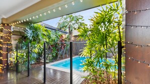 A poolside area with a wooden deck, string lights, and lush greenery. - Modere - Pool Entertainer Child Pet (Cairns)
