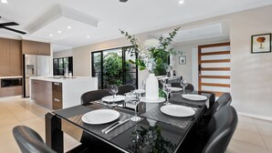 A modern dining area with a glass table, black chairs, and a white centerpiece. - Modere - Pool Entertainer Child Pet (Cairns)