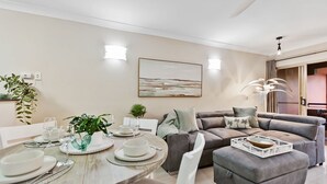 Ein modernes Wohnzimmer mit einem grauen Sofa, einem Esstisch mit Tellern und Gläsern sowie einem großen abstrakten Gemälde an der Wand.
