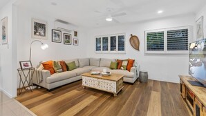 A modern living room with a sectional sofa, a wooden coffee table, and a television. - Curlews Nest - Pool BBQ and Beach (Cairns)