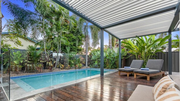 A covered outdoor area with a pool, wooden deck, lounge chairs, and tropical plants. - Curlews Nest - Pool BBQ and Beach (Cairns)