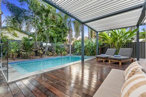 A covered outdoor area with a pool, wooden deck, lounge chairs, and tropical plants. - Curlews Nest - Pool BBQ and Beach (Cairns)