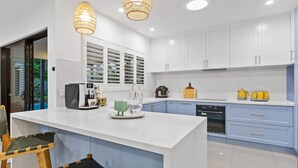 A modern kitchen with white cabinets, a marble island, and a coffee station. - Curlews Nest - Pool BBQ and Beach (Cairns)