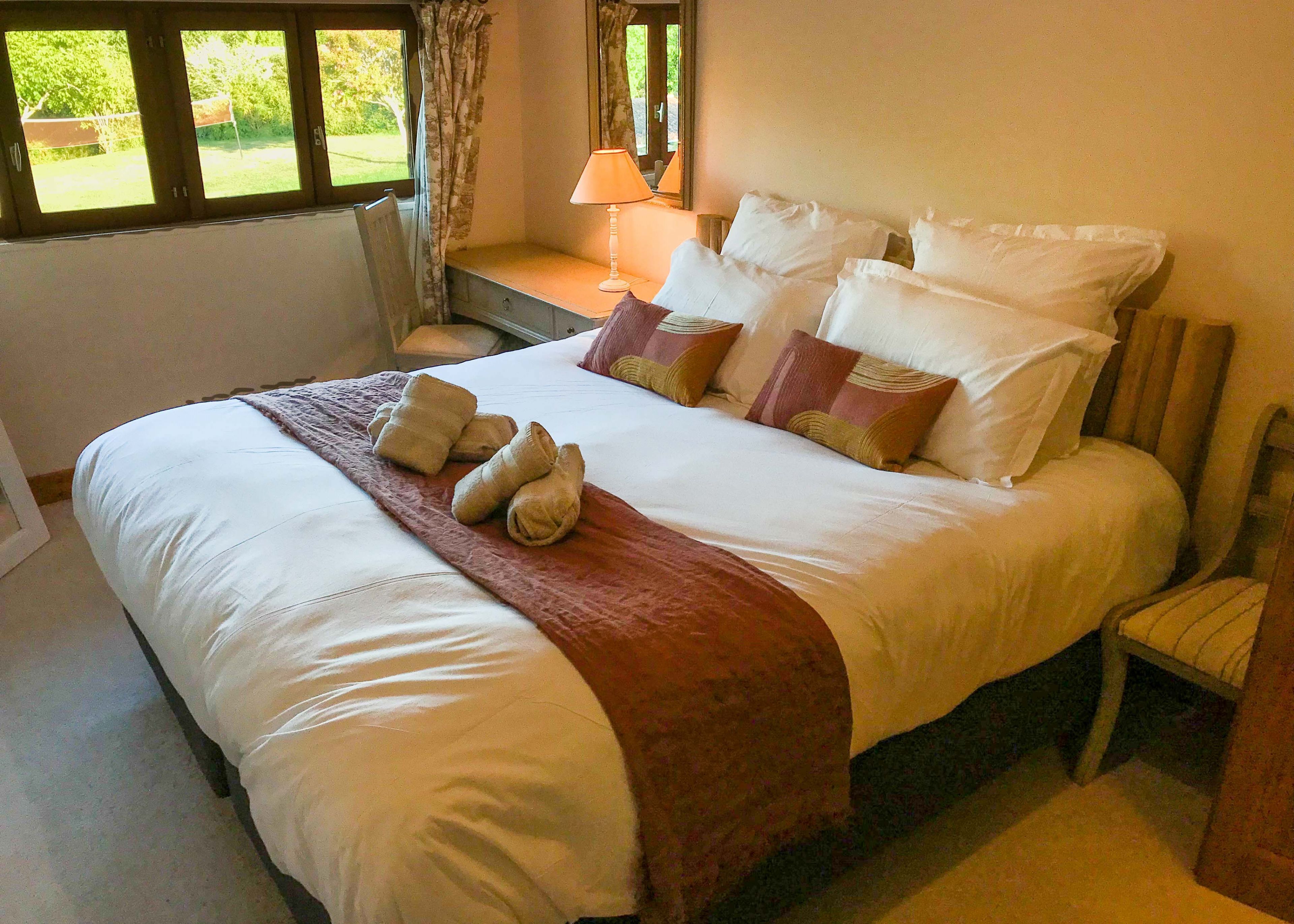 A neatly made bed with a white and brown bedspread, several pillows, and a set of towels on the bed.