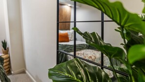 Une pièce avec un lit, une plante et un miroir qui reflète la pièce.