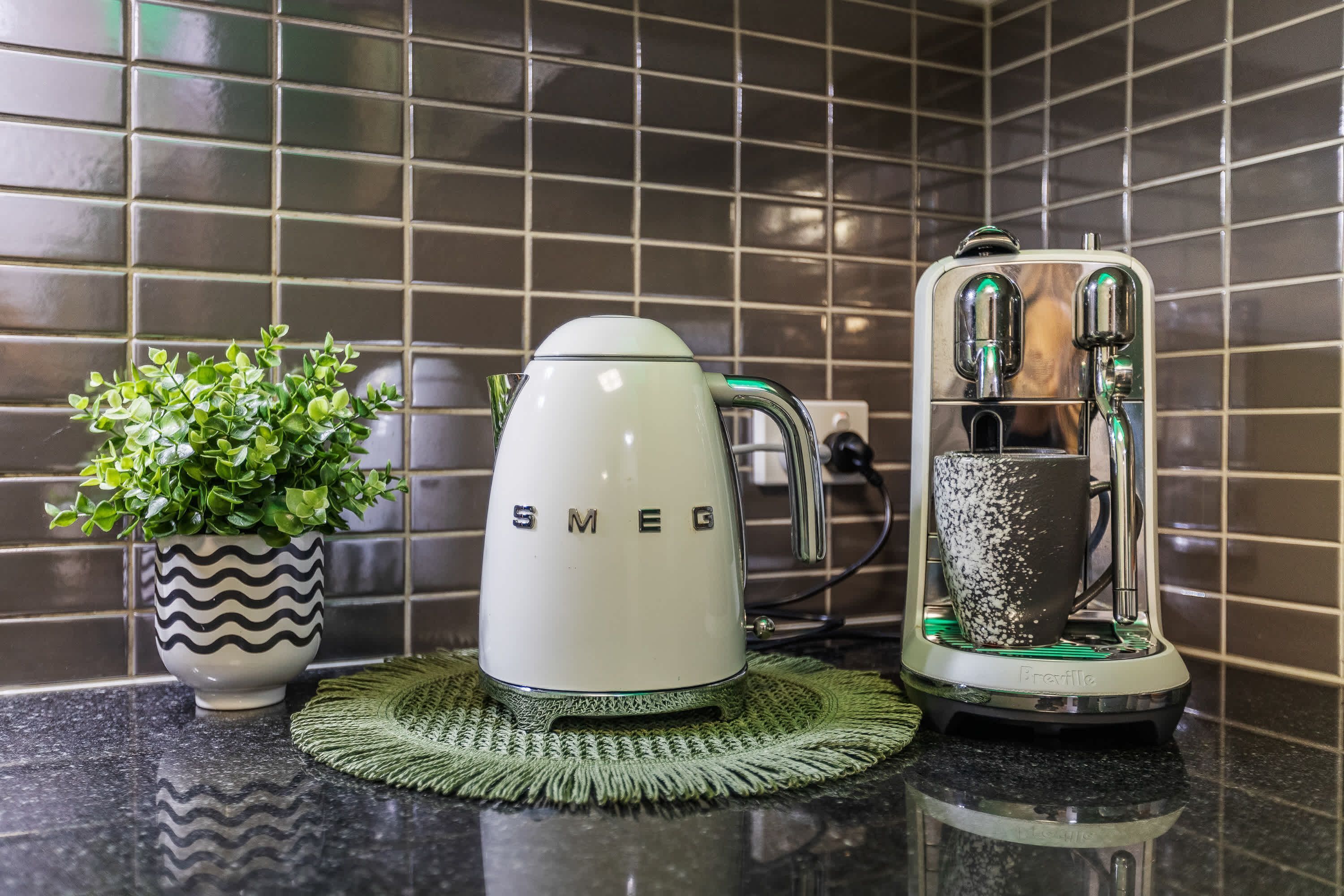 A kitchen with a white Smeg kettle, a Breville coffee maker, and a potted plant on a black countertop.