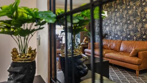 Un salon avec un canapé en cuir marron, un papier peint à motifs et une statue décorative.
