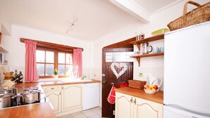 A kitchen with wooden cabinets, a white refrigerator, and a window with pink curtains. - L'Ecurie - The original farmer's cottage (Larzac)