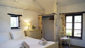 Une chambre à coucher avec un lit, une table de chevet avec une lampe, une chaise et une fenêtre avec des rideaux.