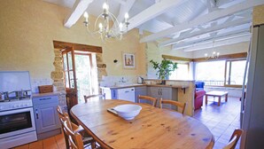 A spacious kitchen with a wooden dining table, built-in appliances, and a view to the outside. - La Grange - sleeps 6 guests  in 3 bedrooms (Larzac)