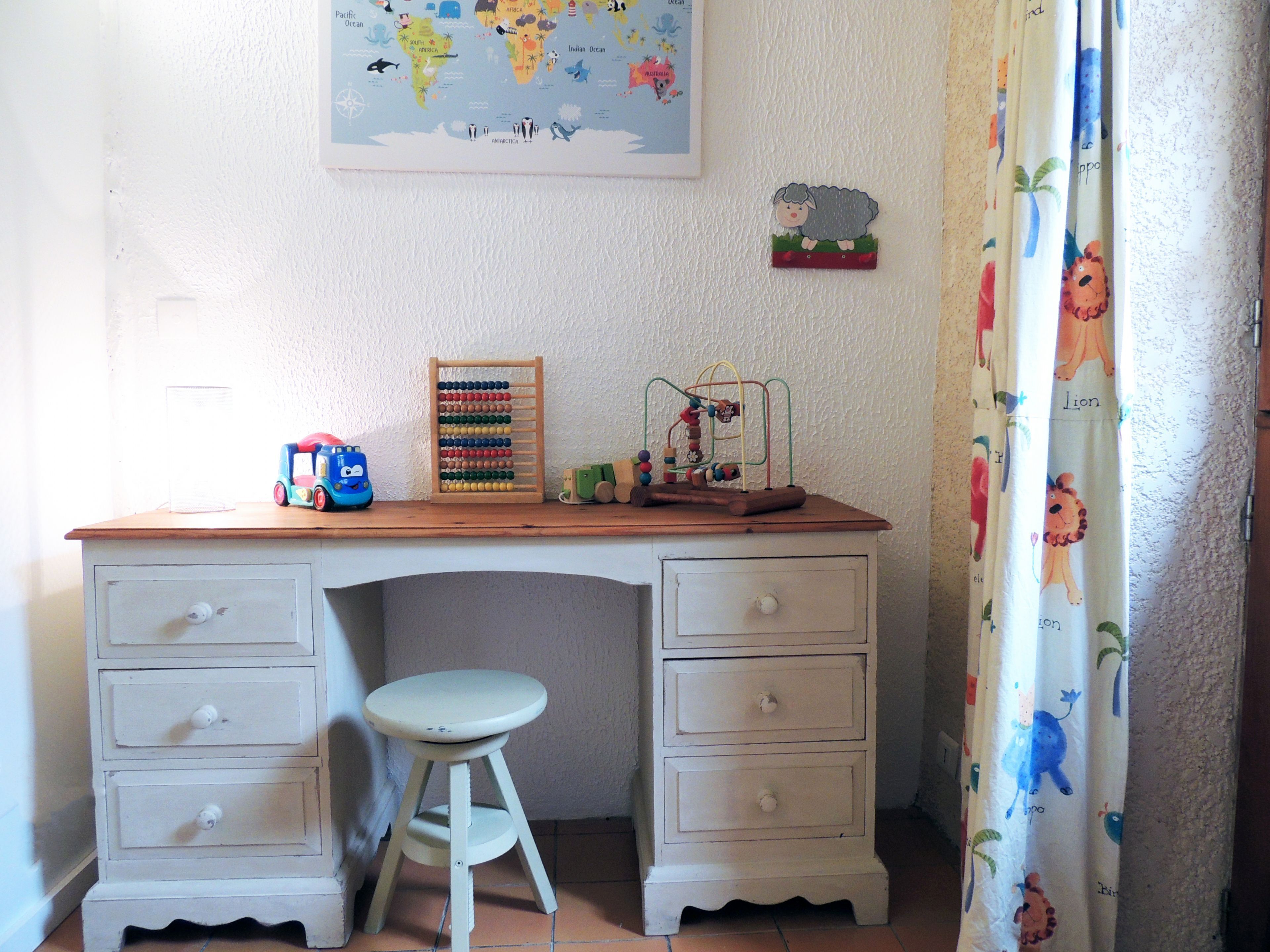 A child's desk with drawers, a toy car, a wooden abacus, and a hanging ornament.
