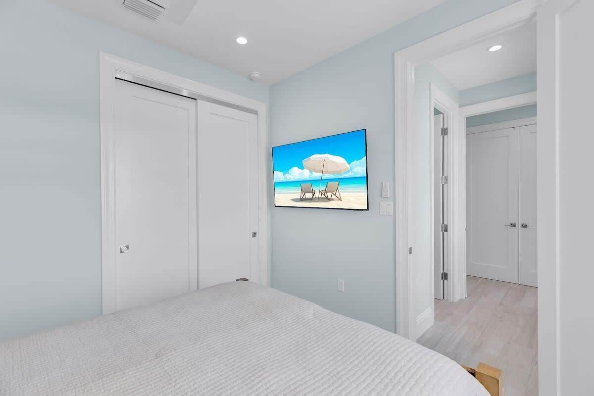 A bedroom with a large bed, a ceiling fan, and a wall-mounted TV displaying a beach scene.