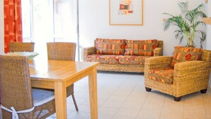 Ein Wohnzimmer mit Korbmöbeln, einem Esstisch und einer Topfpflanze.