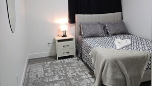 Un dormitorio con cama, una mesita de noche con lámpara, un espejo y una alfombra estampada.