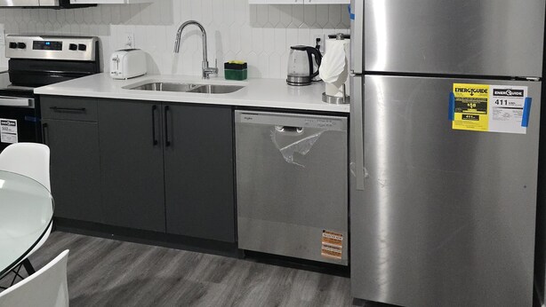 Una cocina moderna con electrodomésticos de acero inoxidable, armarios blancos y suelo gris.