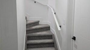 Una escalera con peldaños alfombrados y un pasamanos blanco, que conduce a una puerta blanca.