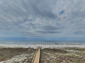 A beach with a wooden boardwalk leading to the water, sandy beach, and a cloudy sky.